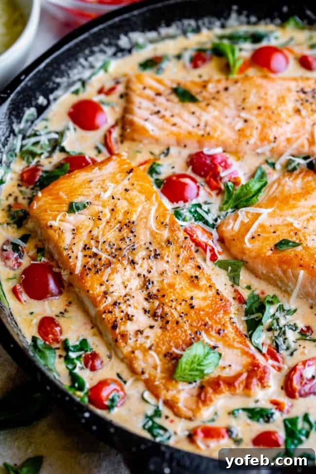 Creamy Tuscan Salmon (30 Minute Dinner!) from The Food Charlatan. This Creamy Tuscan Salmon recipe is totally restaurant quality, but super easy to make! Perfectly pan-seared salmon, drowning in a creamy parmesan sauce with garlic, cherry tomatoes, spinach, and fresh basil. It's the perfect summer meal and is done in 30 minutes! #easy #recipe #summer #garden #salmon #tuscan #creamy #cherrytomato #basil #spinach #parmesan #tomato #30minutedinner #oneskillet #garlic #butter #garlicbutter #pasta creamy Tuscan salmon presented beautifully in a skillet, adorned with bright red cherry tomatoes, dark green spinach, and fresh basil leaves.