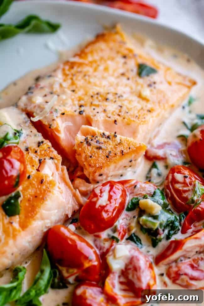 Creamy Tuscan Salmon (30 Minute Dinner!) from The Food Charlatan. This Creamy Tuscan Salmon recipe is totally restaurant quality, but super easy to make! Perfectly pan-seared salmon, drowning in a creamy parmesan sauce with garlic, cherry tomatoes, spinach, and fresh basil. It's the perfect summer meal and is done in 30 minutes! #easy #recipe #summer #garden #salmon #tuscan #creamy #cherrytomato #basil #spinach #parmesan #tomato #30minutedinner #oneskillet #garlic #butter #garlicbutter #pasta a mouth-watering shot of Tuscan butter salmon, adorned with bright cherry tomatoes, fresh spinach, and fragrant basil, ready to be enjoyed.