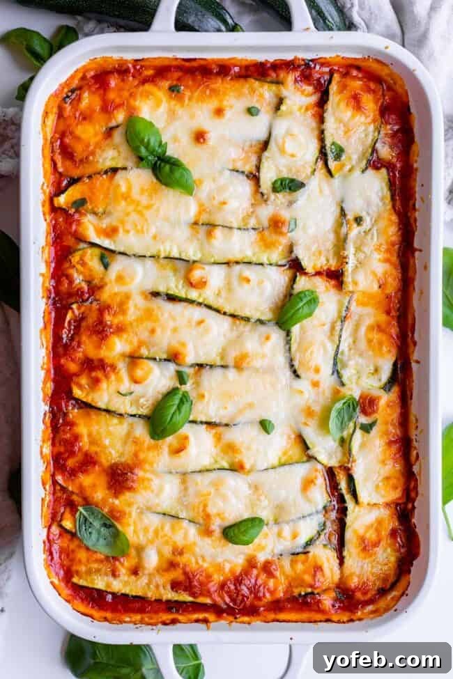 A beautifully baked zucchini lasagna recipe in a white casserole dish, garnished with fresh basil. The dish is full of Italian sausage, marinara sauce, ricotta, and mozzarella, with zucchini slices acting as the lasagna noodles. It is low carb, keto-friendly, and seriously delicious, offering a healthy alternative to pasta-heavy dinners. The recipe focuses on the salting method to remove excess water from the zucchini, making it much easier than grilling or par-baking.