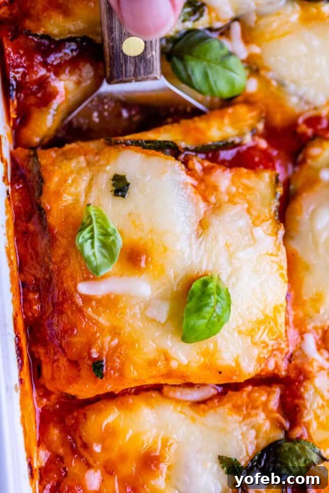 An overhead shot of zucchini lasagna, expertly sliced in the pan, revealing its delectable layers of zucchini, Italian sausage, marinara, ricotta, and mozzarella. This low-carb, keto-friendly recipe offers a healthy alternative to traditional pasta-heavy dinners, utilizing the efficient salting method to remove excess water from the zucchini, ensuring a perfectly structured and delicious dish.