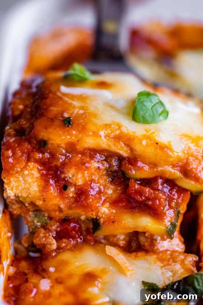 A slice of zucchini lasagna being carefully lifted from the pan on a spatula, revealing its rich, layered interior. This image emphasizes the dish's structural integrity and appetizing presentation, made possible by the careful preparation of zucchini as a low-carb alternative to pasta.
