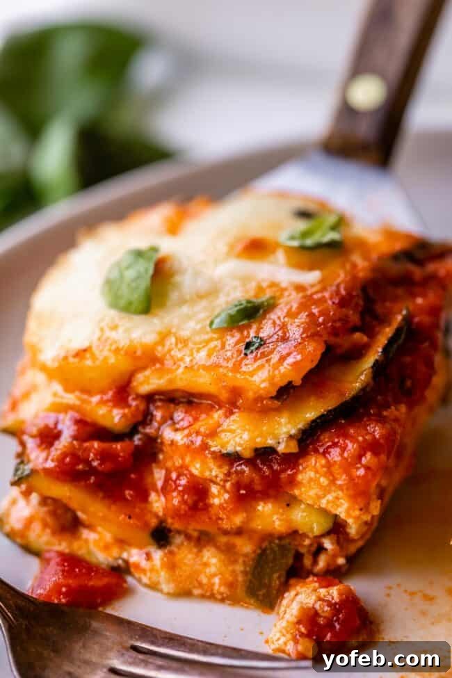 A slice of zucchini lasagna being carefully placed onto a white plate with a spatula, indicating it's ready to be served. This image showcases the well-structured layers of zucchini, Italian sausage, marinara, ricotta, and mozzarella, highlighting the success of the low-carb, keto-friendly recipe.