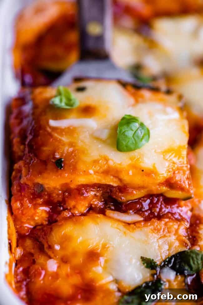 A cheesy slice of zucchini lasagna being lifted from the pan with a spatula, garnished with fresh basil. This low-carb, keto-friendly recipe features Italian sausage, marinara sauce, ricotta, and mozzarella, all layered with zucchini instead of pasta noodles. It's a seriously delicious and healthy alternative, with the zucchini prepared using the salting method for optimal texture and flavor, avoiding a watery result.