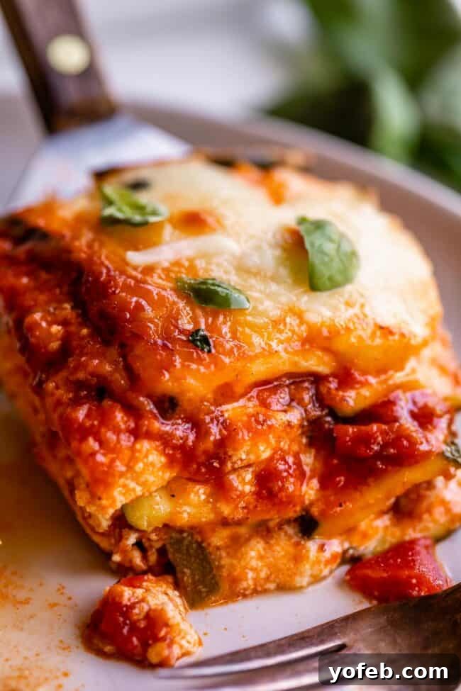 A perfectly portioned slice of zucchini lasagna on a white plate, ready to be enjoyed with a fork, and topped with fresh basil. This low-carb, keto-friendly recipe brilliantly substitutes zucchini for traditional lasagna noodles, creating a seriously delicious meal rich with Italian sausage, marinara sauce, ricotta, and mozzarella. The zucchini is prepared using a straightforward salting method to prevent wateriness, offering a healthier, lighter alternative that doesn't compromise on flavor.
