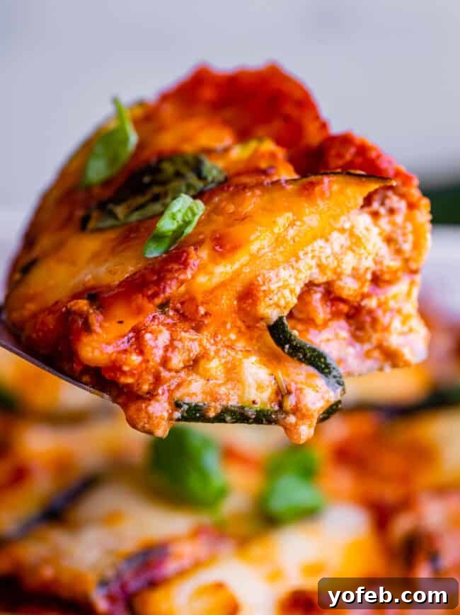 A perfectly portioned slice of cheesy zucchini lasagna is held up on a spatula, showcasing its distinct layers. This low-carb, keto-friendly lasagna features thinly sliced zucchini instead of pasta, complemented by a rich Italian sausage marinara, creamy ricotta, and generous amounts of melted mozzarella. The image emphasizes the appetizing texture and the success of the salting method in removing water from the zucchini, resulting in a firm, delicious slice.