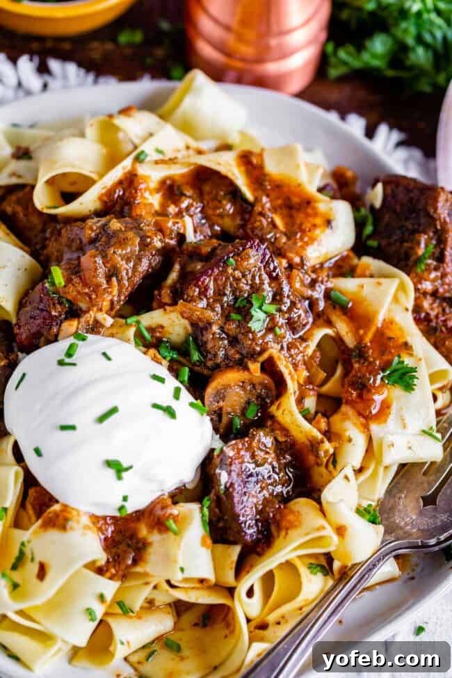 Homestyle Slow Cooker Beef Stroganoff 2 crockpot beef stroganoff served over pappardelle pasta on a plate with sour cream and fresh chives.