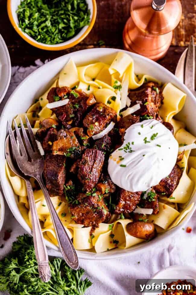 Homestyle Slow Cooker Beef Stroganoff 5 crock pot beef stroganoff with a big dollop of sour cream and fresh chives in a bowl with a fork and spoon.