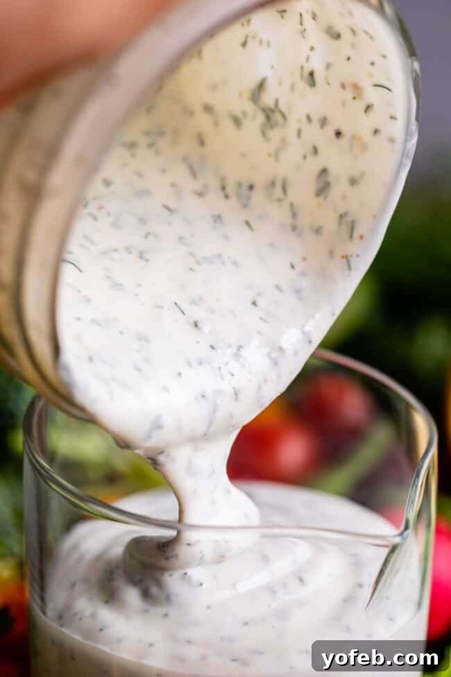 Homemade Buttermilk Ranch Dressing creamy buttermilk ranch recipe being poured from a glass jar into a glass measuring cup.