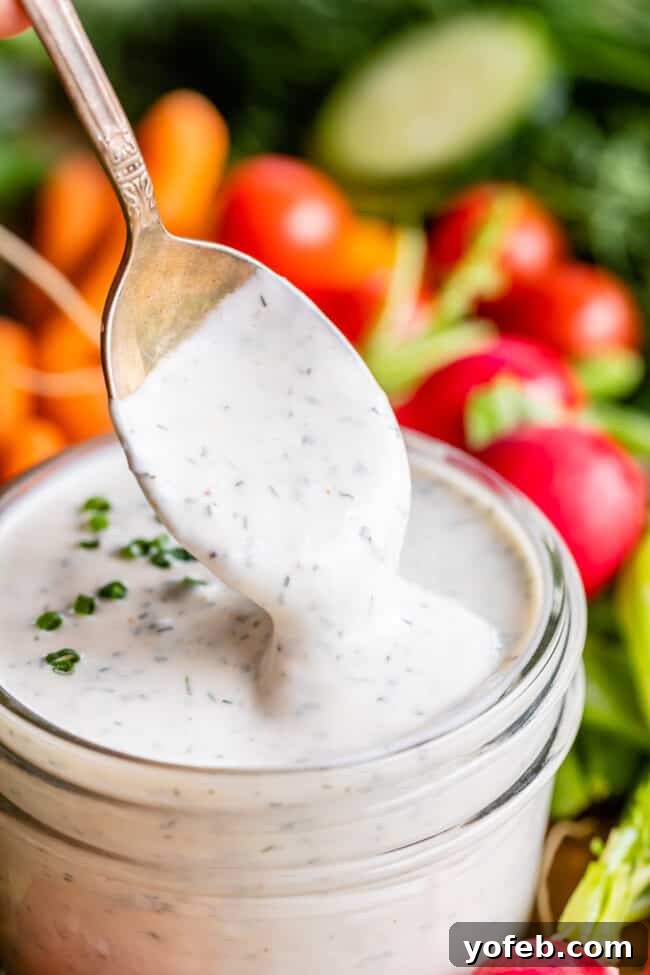 Homemade Buttermilk Ranch Dressing creamy buttermilk ranch dressing with spoon dipping into glass jar with fresh vegetables in the background.