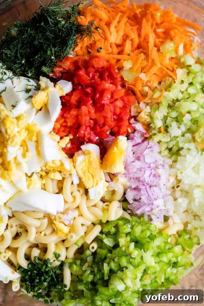 Classic Creamy Macaroni Salad 5 finely chopped ingredients in a bowl, including hard-boiled eggs, colorful bell peppers, carrots, celery, alongside cooked pasta and fresh herbs, ready for mixing into macaroni salad.