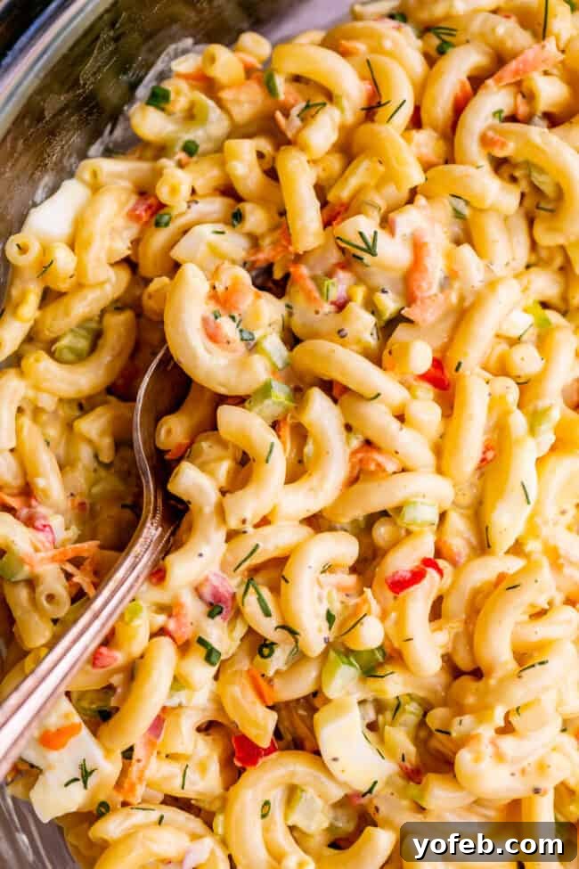 Classic Creamy Macaroni Salad 8 moist macaroni salad in a clear mixing bowl with a serving spoon, highlighting its ideal consistency and readiness to serve.