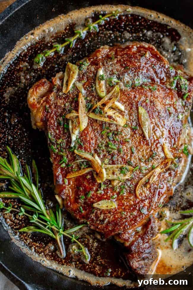 Cooking a ribeye steak in a cast iron pan, enriched with bubbling garlic butter and fresh rosemary sprigs.