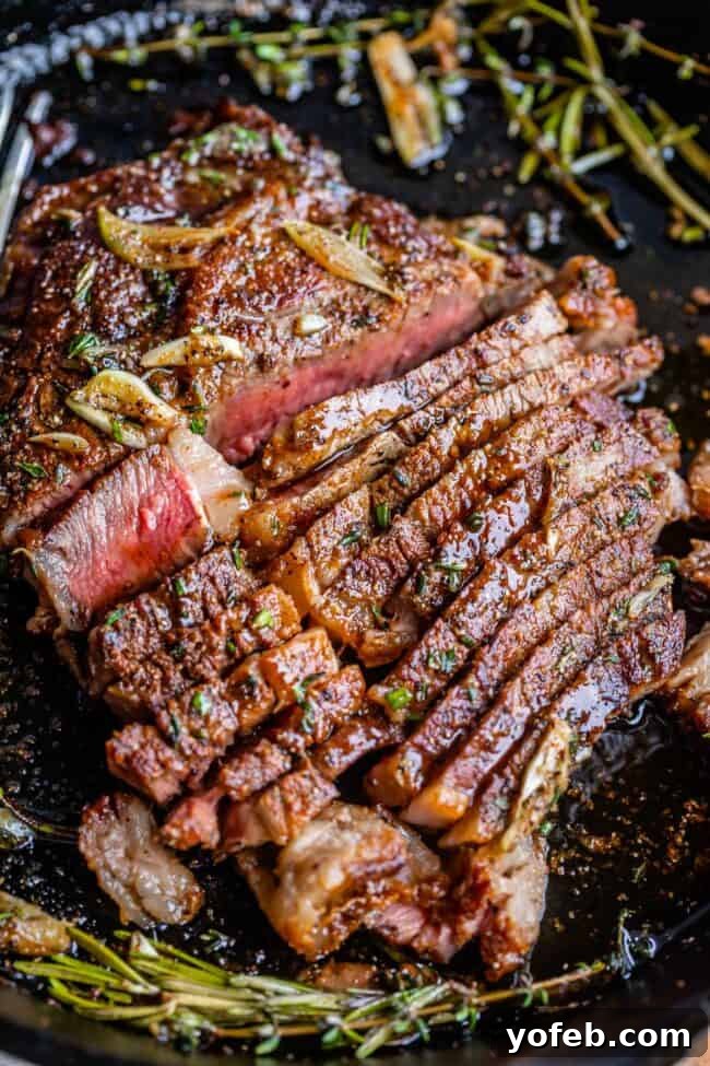 Beautifully sliced grilled ribeye steak resting in a pan, coated in garlic butter and garnished with fresh herbs.