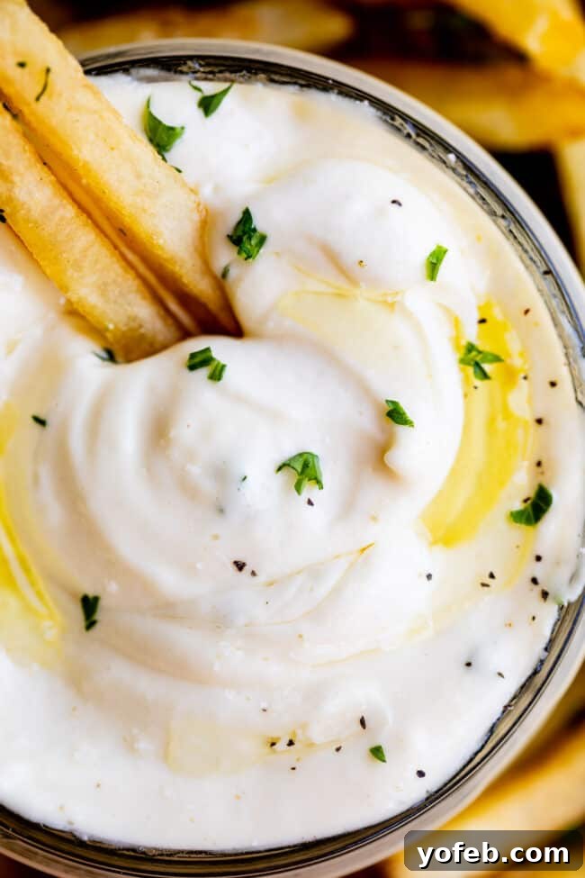 Garlic Aioli Recipe (Classic and Cheater Versions) from The Food Charlatan. Learn to make homemade Garlic Aioli Sauce with ease. Both classic and cheater versions are quick, easy, and result in lemony, garlicky perfection. It's the ideal condiment for fries, veggies, burgers, and more. #recipe #easy #garlic #lemon #aioli #sauce #mayonnaise #roasted #garlicmayo #fromscratch #homemade #creamy Close-up shot of creamy garlic aioli sauce served with crispy golden french fries, ready for dipping.