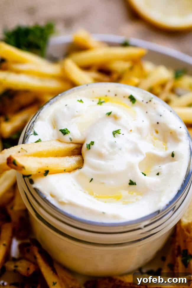 Garlic Aioli Recipe (Classic and Cheater Versions) from The Food Charlatan. I will show you just how easy it is to make homemade Garlic Aioli Sauce! Making it from scratch is quick and easy, but I have a cheater version that is even quicker and easier. Either way you make it, aioli is lemony garlicky heaven! It will be your new favorite condiment in no time. #recipe #easy #garlic #lemon #aioli #sauce #mayonnaise #roasted #garlicmayo #fromscratch #homemade #creamy A glass jar filled with homemade garlic aioli sauce, surrounded by a generous serving of crispy french fries.