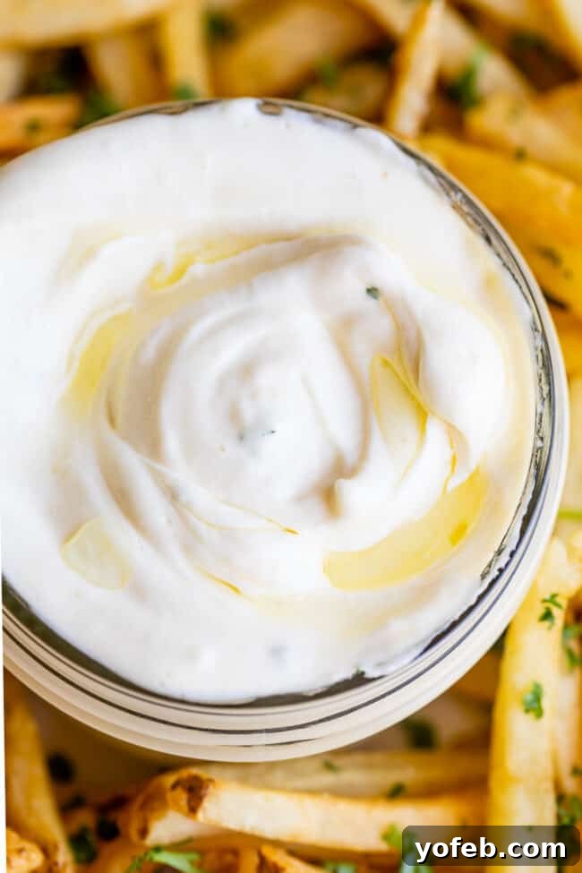Garlic Aioli Recipe (Classic and Cheater Versions) from The Food Charlatan. I will show you just how easy it is to make homemade Garlic Aioli Sauce! Making it from scratch is quick and easy, but I have a cheater version that is even quicker and easier. Either way you make it, aioli is lemony garlicky heaven! It will be your new favorite condiment in no time. #recipe #easy #garlic #lemon #aioli #sauce #mayonnaise #roasted #garlicmayo #fromscratch #homemade #creamy A close-up of golden french fries generously seasoned with herbs, served with a side of creamy garlic aioli.