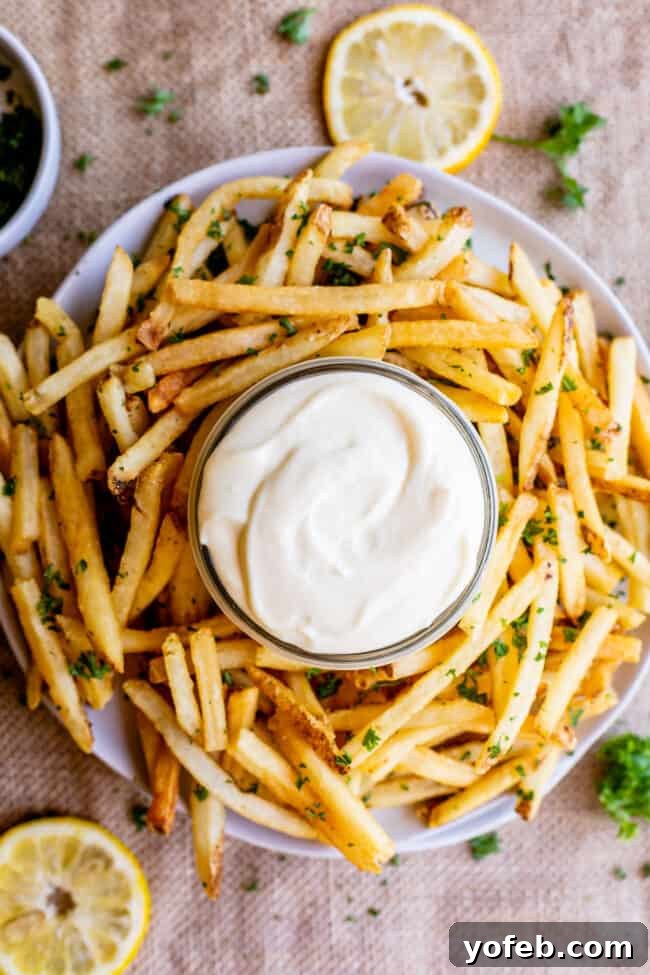 Garlic Aioli Recipe (Classic and Cheater Versions) from The Food Charlatan. I will show you just how easy it is to make homemade Garlic Aioli Sauce! Making it from scratch is quick and easy, but I have a cheater version that is even quicker and easier. Either way you make it, aioli is lemony garlicky heaven! It will be your new favorite condiment in no time. #recipe #easy #garlic #lemon #aioli #sauce #mayonnaise #roasted #garlicmayo #fromscratch #homemade #creamy A jar of homemade garlic aioli sauce positioned next to a plate piled high with crispy french fries.