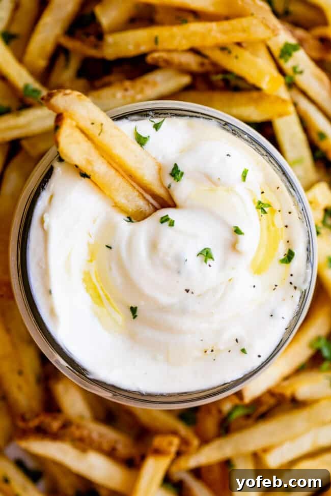 Garlic Aioli Recipe (Classic and Cheater Versions) from The Food Charlatan. I will show you just how easy it is to make homemade Garlic Aioli Sauce! Making it from scratch is quick and easy, but I have a cheater version that is even quicker and easier. Either way you make it, aioli is lemony garlicky heaven! It will be your new favorite condiment in no time. #recipe #easy #garlic #lemon #aioli #sauce #mayonnaise #roasted #garlicmayo #fromscratch #homemade #creamy Overhead shot of a small bowl of garlic aioli accompanied by a plate of crispy french fries.
