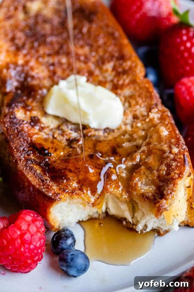 Golden Glazed French Toast 15 Thick French toast on a plate with fresh raspberries, strawberries, blueberries, a pat of butter, and a drizzle of syrup.