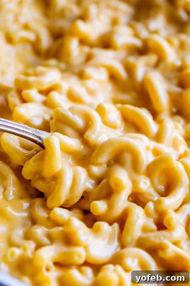 Creamy Homemade Velveeta Mac and Cheese 12 A serving of super creamy mac and cheese resting in a wide pan, with a large spoon ready to scoop, highlighting its inviting and rich texture.