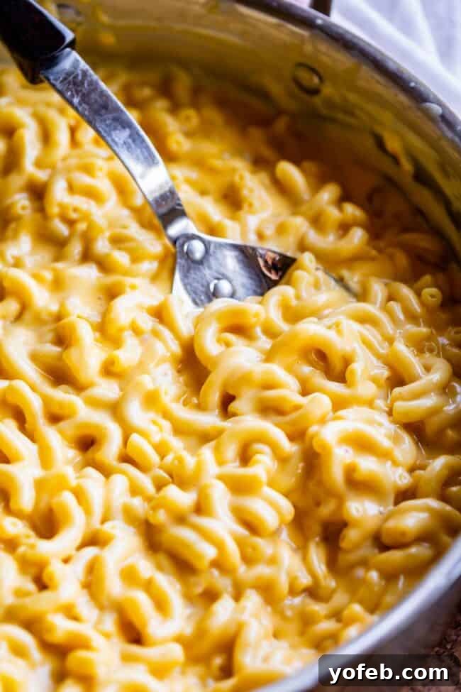 Creamy Homemade Velveeta Mac and Cheese 7 A large serving spoon lifts a generous portion of homemade mac and cheese directly from a wide, shallow pan, emphasizing its one-pot preparation and creamy consistency.