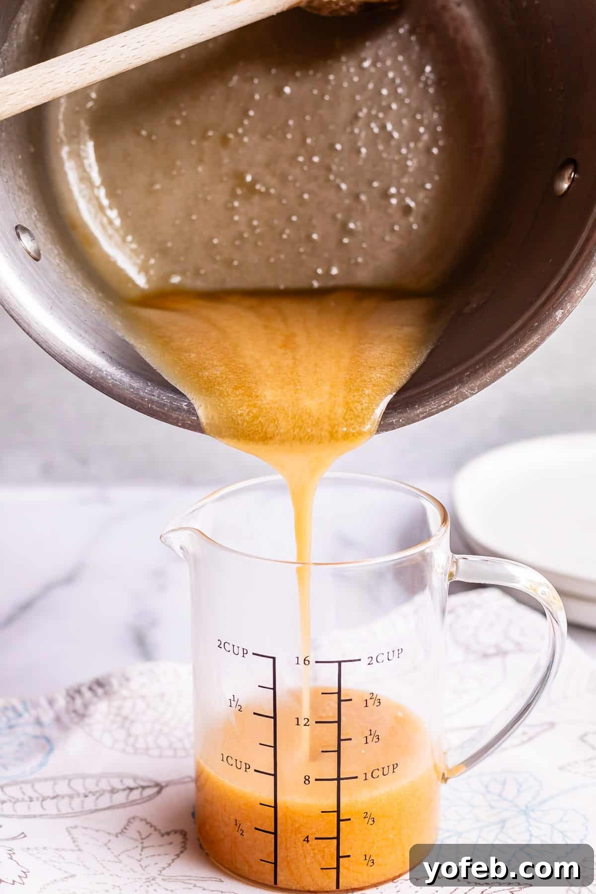 Velvet Smooth Buttermilk Syrup 13 pouring syrup from a pot into a glass measuring cup on a white counter.