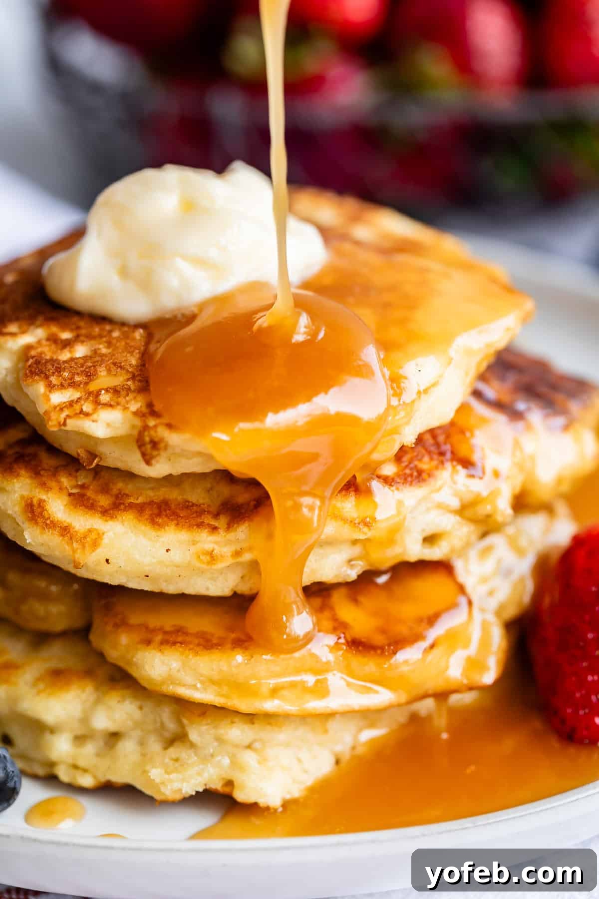 Velvet Smooth Buttermilk Syrup 5 pouring buttermilk syrup over a stack of pancakes with butter and strawberry.