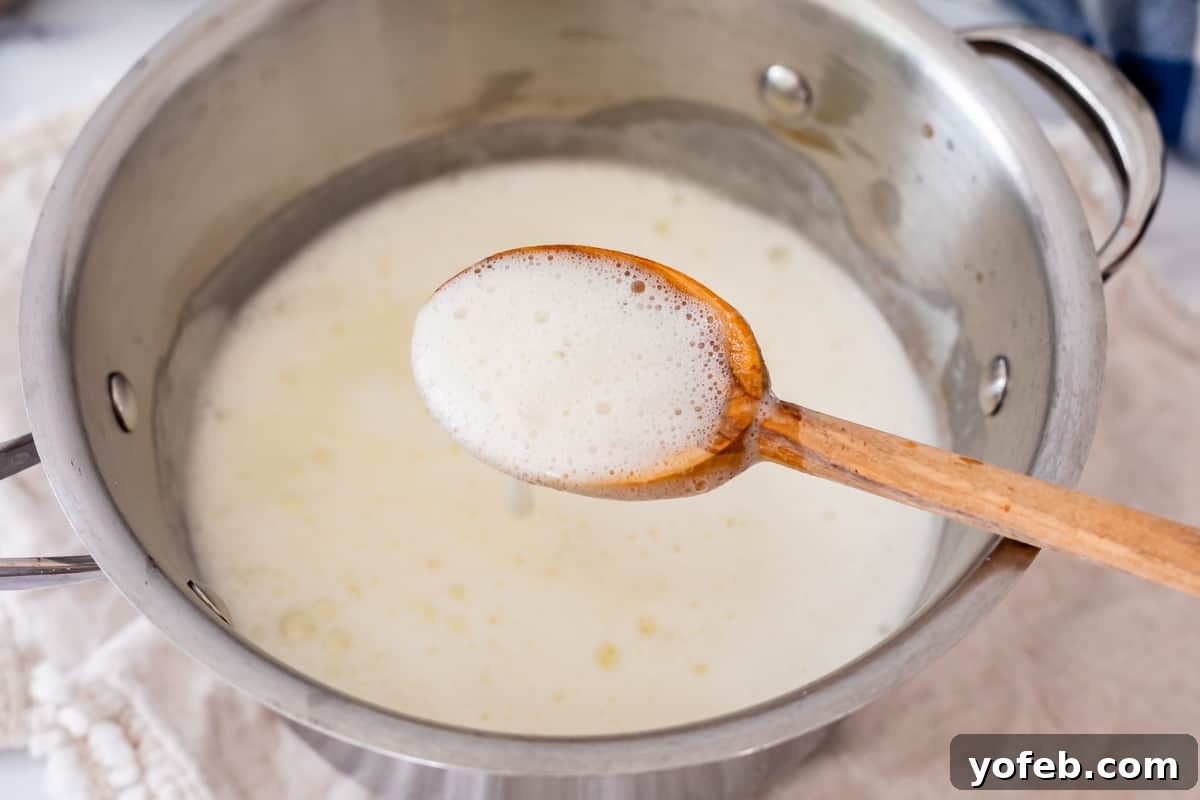 Velvet Smooth Buttermilk Syrup 10 wooden spoon holding up bubbly white syrup from a metal spoon.