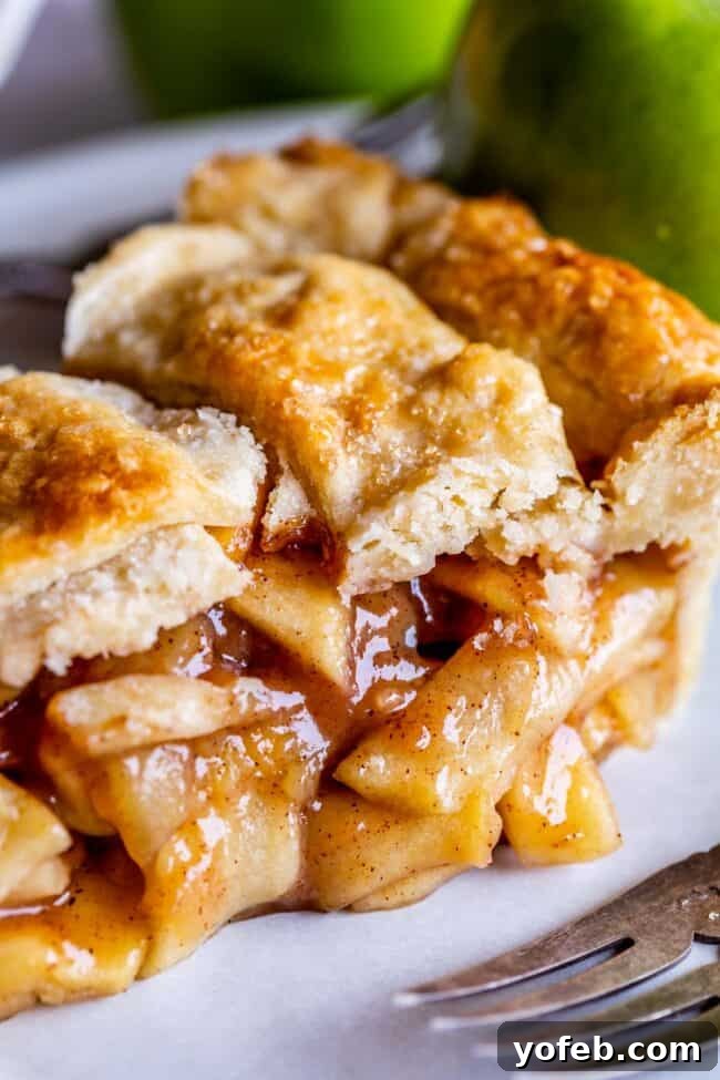 A delectable slice of apple pie, featuring a golden, homemade flaky pie crust, resting beside a gleaming metal fork.