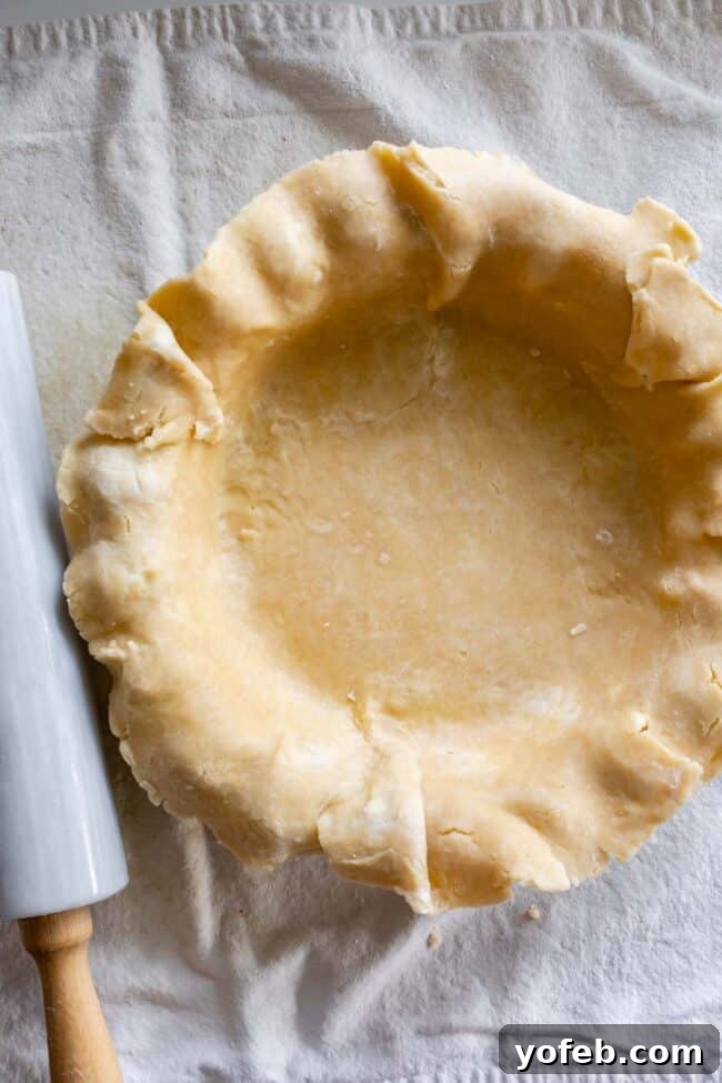 A pristine, never-fail flaky pie crust beautifully settled in a pie pan, with a rolling pin resting nearby, indicating its readiness.
