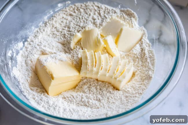 Cold butter and shortening cubes are placed in a bowl of flour, poised for blending, showcasing the key fats for a flaky pie crust.