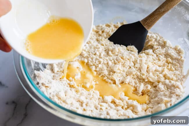 A mixture of egg and ice water being poured into pie crust dough, demonstrating the liquid addition step.