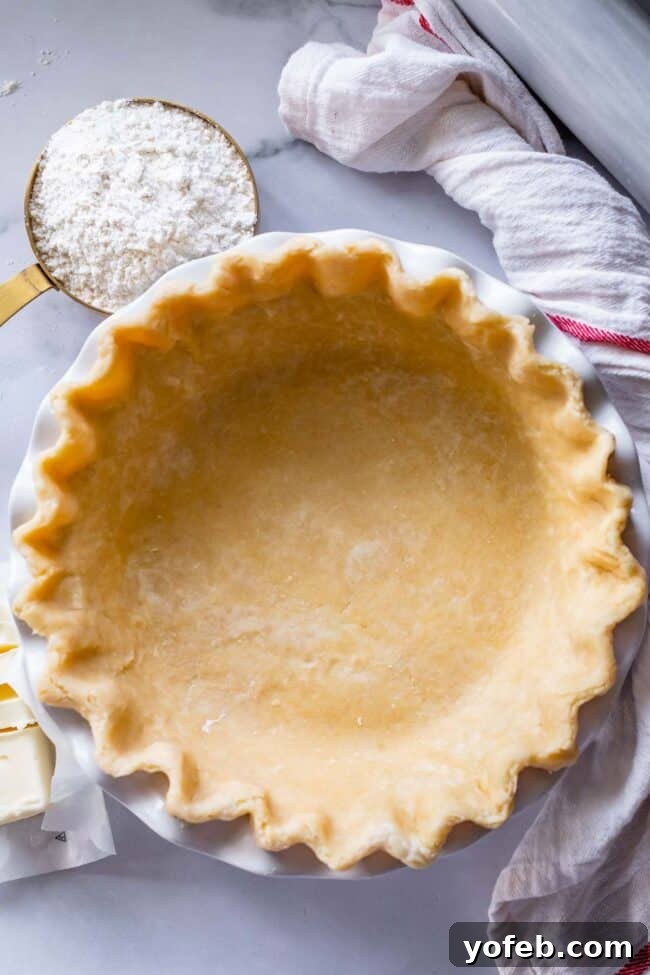 How to Pre-Bake Your Pie Crust Perfectly 2 A beautifully fluted pie shell, perfectly shaped and ready for blind baking, resting in a ceramic pie dish. The edges are crimped meticulously, promising a professional finish.