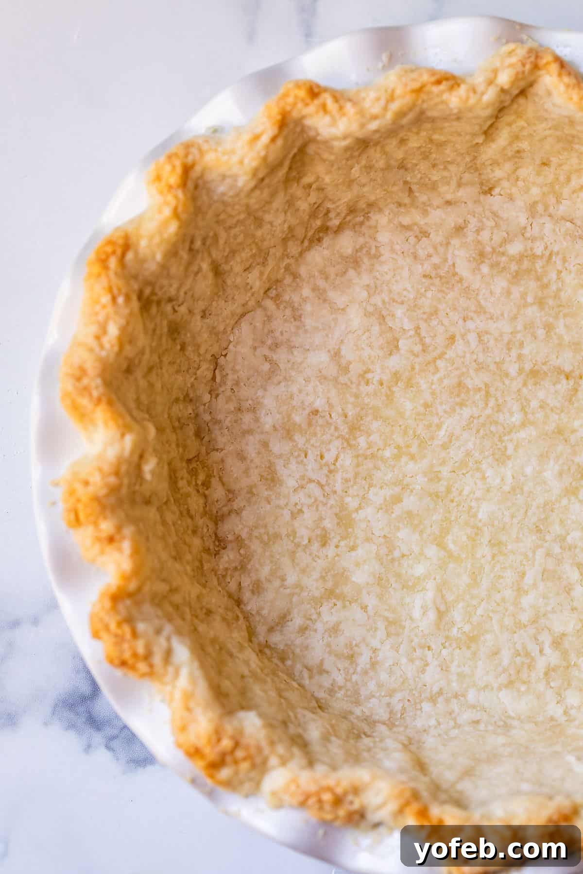 How to Pre-Bake Your Pie Crust Perfectly 11 An overhead shot of a par-baked pie crust in a white pie dish, sitting on a counter. The bottom of the crust is matte and light in color, indicating it's partially cooked and no longer shiny or raw.