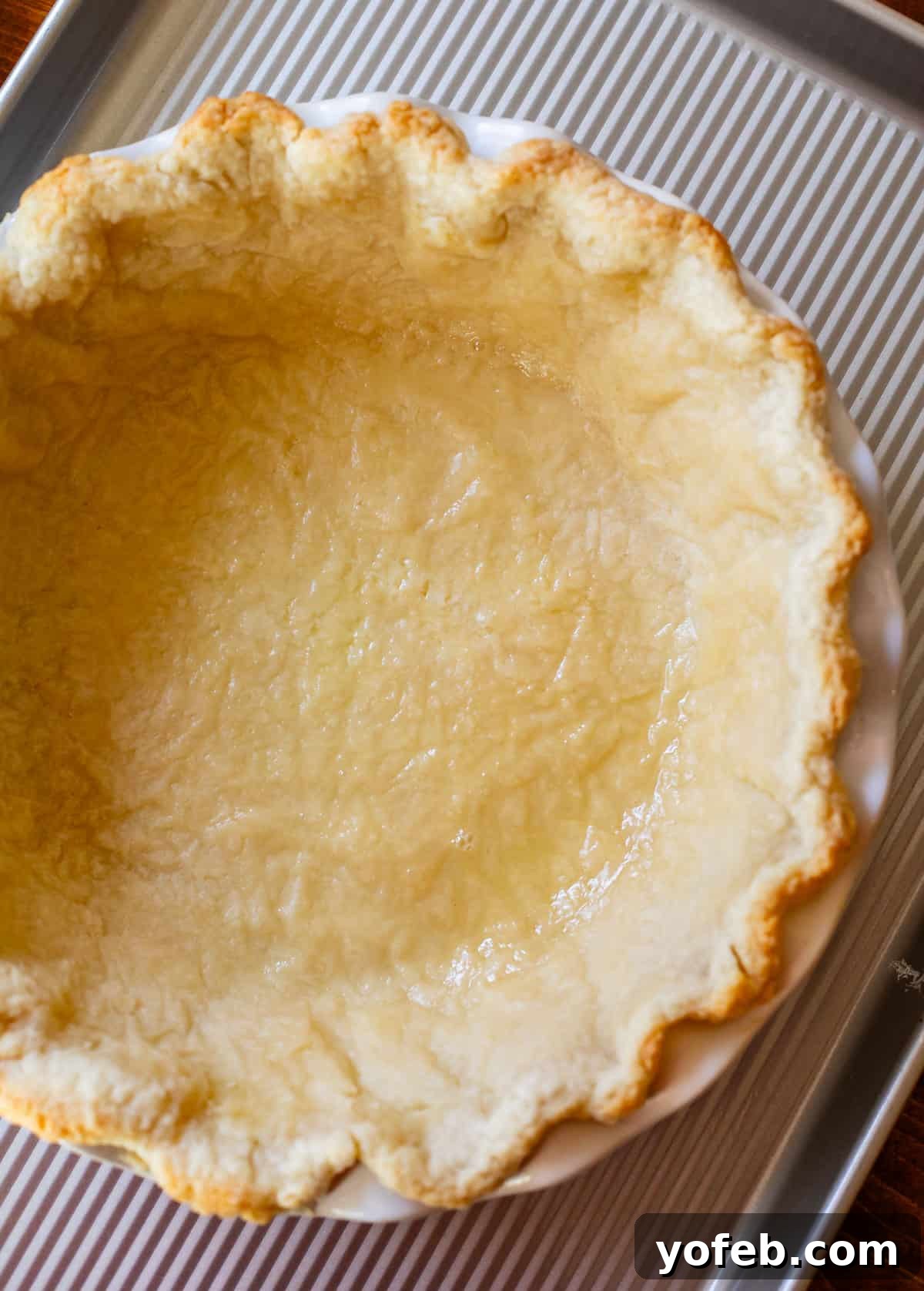 How to Pre-Bake Your Pie Crust Perfectly 10 A half-baked pie crust in a white pie pan, resting on a baking sheet. The edges are lightly browned, but the bottom still appears uncooked and pale, awaiting its second bake.