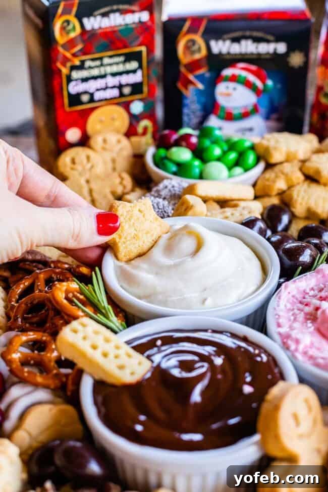 Sweet Grazing Boards 7 A hand dipping a piece of Walkers Shortbread into a fluffy marshmallow creme dip on a festive dessert charcuterie board, surrounded by other sweets.