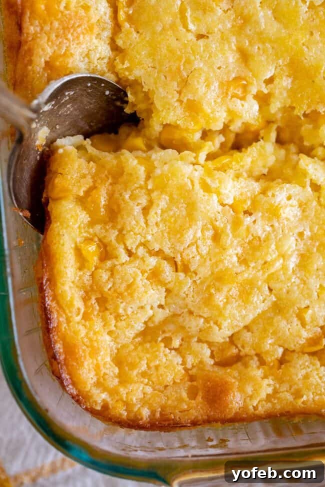 Golden Cornbread Delight 13 creamed corn casserole in a pan with a spoon.