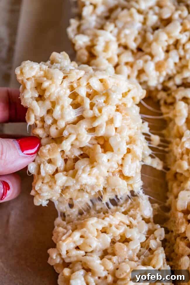 Foolproof Rice Krispies Treats 15 Homemade Rice Krispie Treats being pulled from the pan with fingers, showing stickiness.