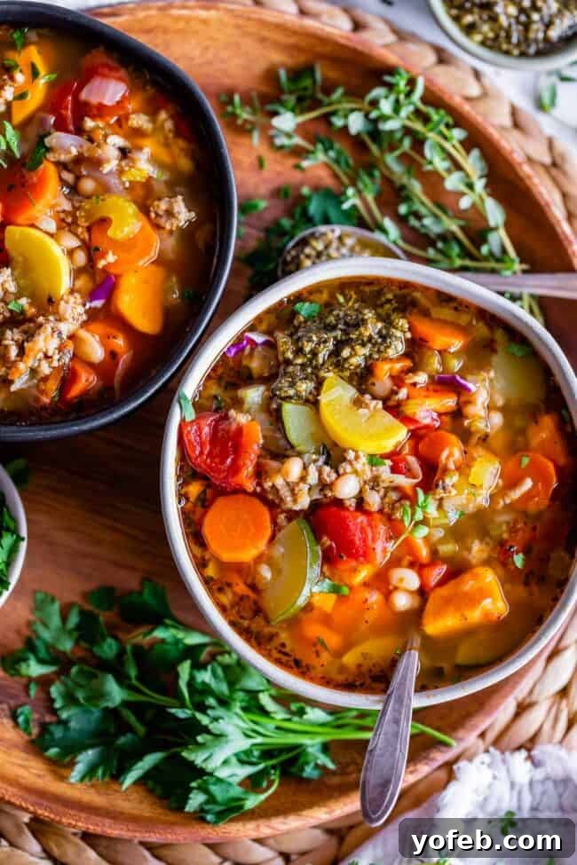 Two bowls of comforting Ground Turkey Vegetable Soup, adorned with fresh herbs, resting on a rustic wooden charger plate.