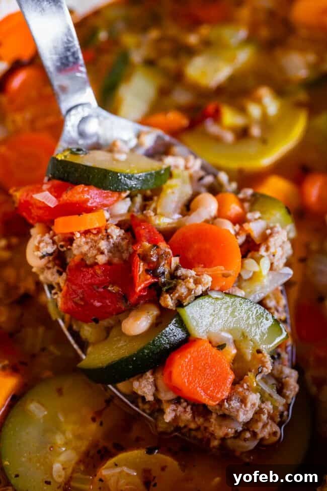 A ladle lifts a spoonful of rich, homemade Turkey Vegetable Soup from a pot, showcasing its abundance of ingredients.