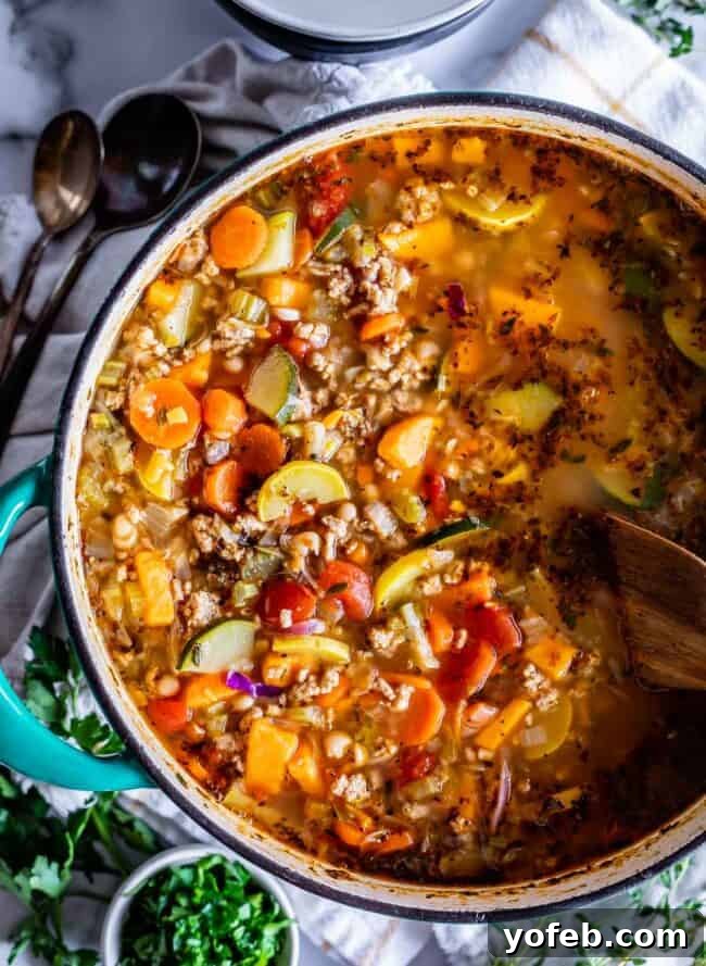 Overhead shot of Turkey Vegetable Soup simmering in a pot with a wooden spoon, indicating freshness and warmth.