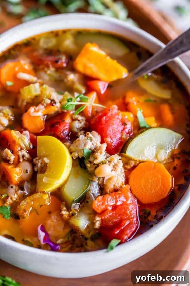 A close-up shot of a white bowl filled with savory Turkey Vegetable Soup, served with a spoon.
