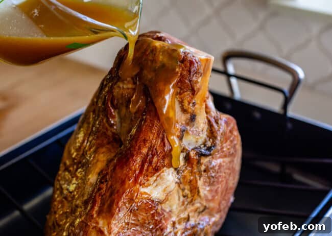 Ultimate Honey Baked Ham 7 Pouring homemade honey glaze over a spiral ham on a roasting rack.