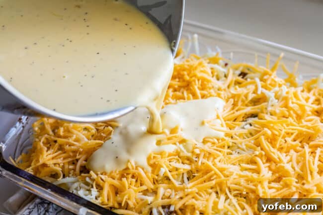 The Ultimate Sausage Breakfast Casserole 10 pouring egg mixture over a cheesy casserole.