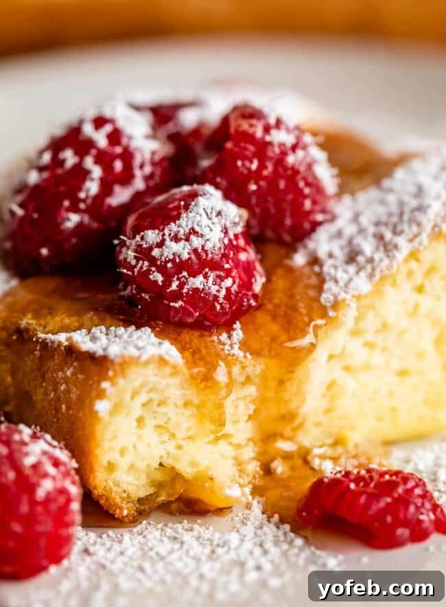 a fluffy german pancake with syrup, powdered sugar, and raspberries.