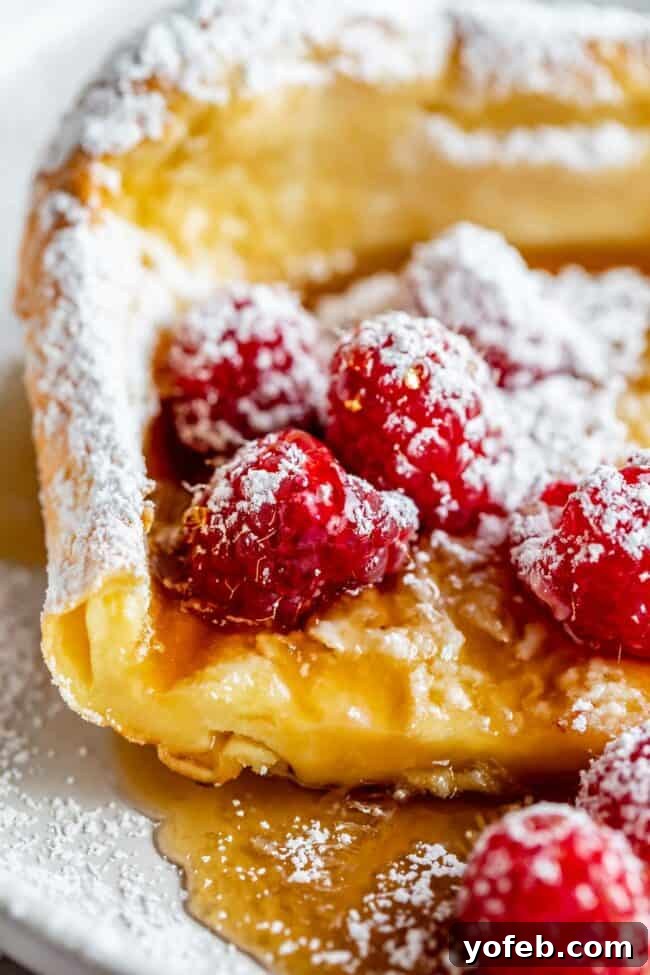 dutch baby with raspberries, syrup, and powdered sugar.