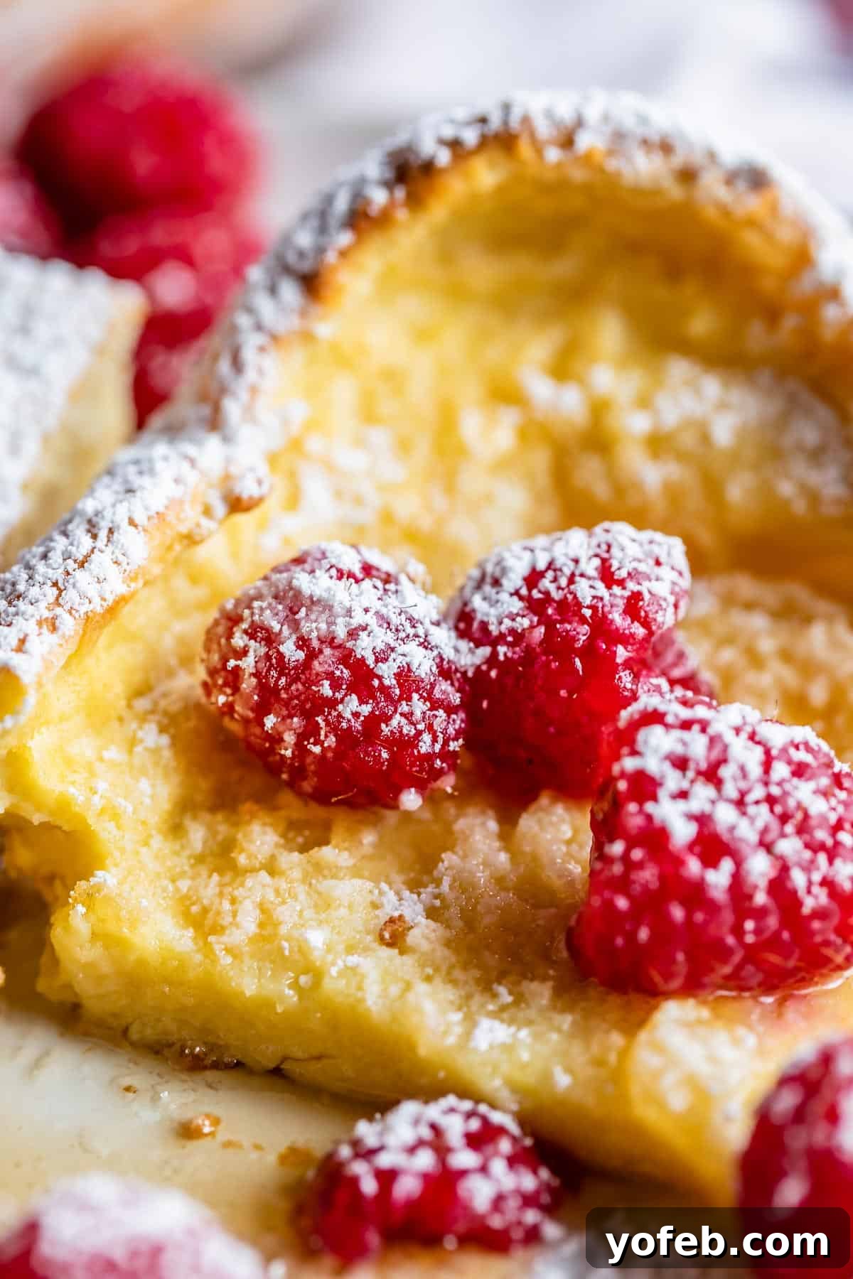 puffy pancakes on a plate with raspberries and powdered sugar.