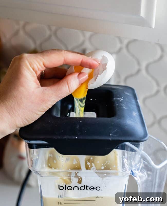 cracking an egg into batter that's in a blender.