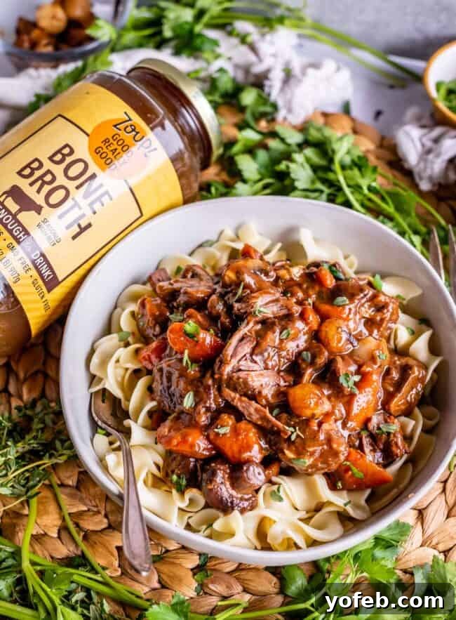 Classic French Beef Bourguignon 11 A comforting bowl of egg noodles generously topped with Beef Bourguignon, served alongside a glass jar of Zoup! Broth, highlighting the quality ingredient used in the dish.