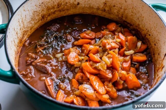 Classic French Beef Bourguignon 20 Sautéed carrots being carefully added to a simmering pot of Beef Bourguignon, enriching the stew with vibrant color and tender texture.